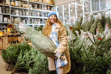 Young woman wearing hat selects Christmas tree at market. Joyful woman, enjoying festive spirit in warm coat and hat, chooses tree for holiday. Concepts of consumerism, celebration, and marketplace.