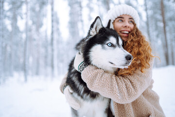 A beautiful woman is having fun with her Siberian husky in a winter forest. A young woman and her dog are enjoying the snowy forest. Concept of friendship, fun, and relaxation. Lifestyle.