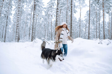 A beautiful woman is having fun with her Siberian husky in a winter forest. A young woman and her dog are enjoying the snowy forest. Concept of friendship, fun, and relaxation. Lifestyle.