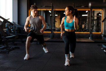 Sporty man and woman doing lunges exercises, warming up and burning leg muscles, exercising in modern gym interior