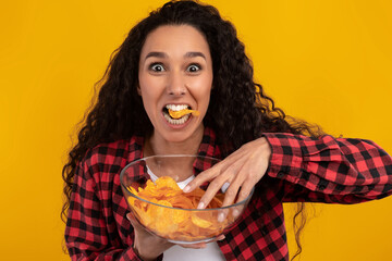 A joyful Latin woman is having a great time eating potato crisps.