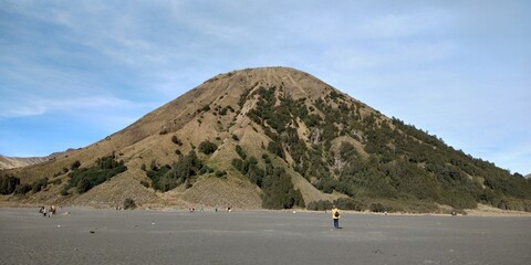 a small mountain near bromo crater with rocky structure, sparse trees, and sandy environment