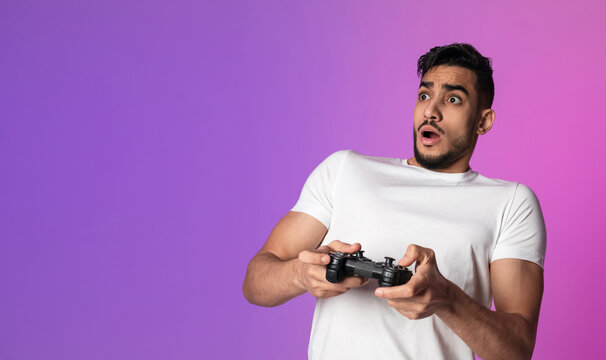 A surprised young Arab man holds a joystick, immersed in an online gaming competition. Neon lights create a vibrant atmosphere as he reacts to an unexpected game event.