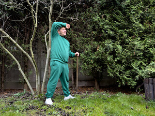 Man in green tracksuit in garden with stick