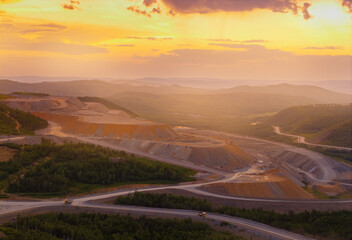 Fototapeta premium Aerial view of expansive open pit mine at sunset with stunning horizon and forested landscape