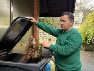 Man disposing of potted plant in trash bin