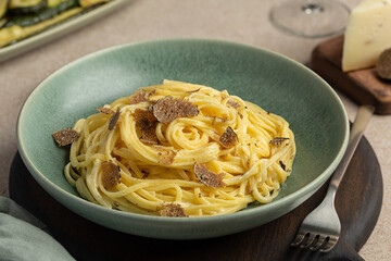 Close up of Plate of Italian egg pasta with black truffle, or Tagliolini al Tartufo Nero. Beige table surface.