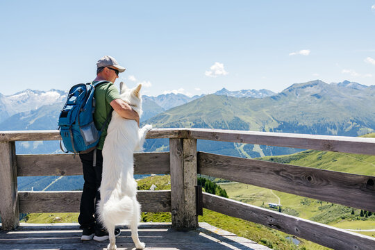 Hiker embracing white swiss shepherd dog enjoying scenic mountain view
