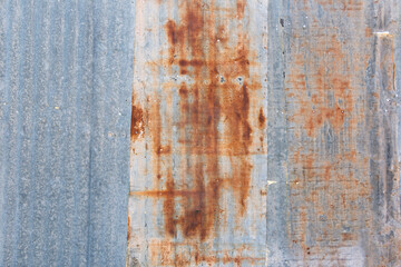 Rusty corrugated metal panels are recycled by piecing them together into a colorful fence. The colors are gray and shades of brown, and the pattern is striped. Horizontal orientation. 