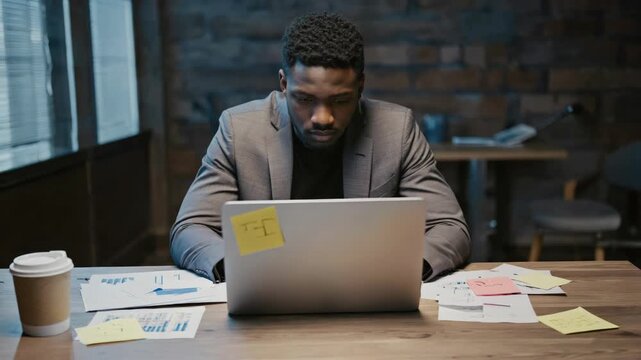 A man in a suit looking at notes and laptop