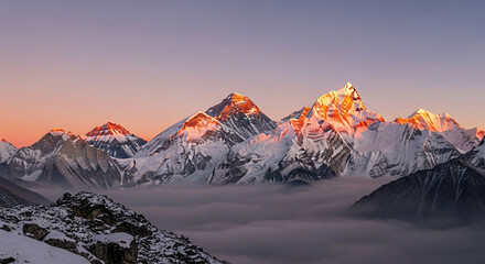 Scenic mountain range with snow-capped peaks illuminated by sunlight, rising above clouds, representing natural grandeur and inspiring adventure