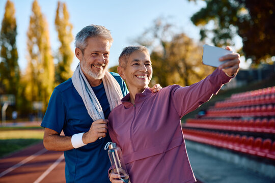 Happy mature sports couple taking selfie while exercising outdoors.