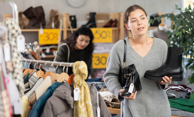 European woman stands in a shoe store and chooses heeled ankle boots and platform boots. Woman buying shoes on sale in a store