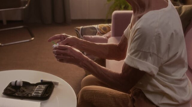 Medium side shot of senior Caucasian woman with diabetes, autoimmune health condition, controlling blood sugar at home by inserting test strip into glucose meter and looking at readings
