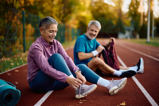 Mature sportswoman tying shoelaces while preparing for outdoor workout in autumn.