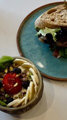 Close-up of a healthy breakfast bowl with fresh fruit, nuts, and yogurt next to a sandwich on a ceramic plate in a modern café