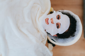 A serene facial treatment scene where a person rests under a soft blanket, wearing a revitalizing sheet mask in a tranquil spa.