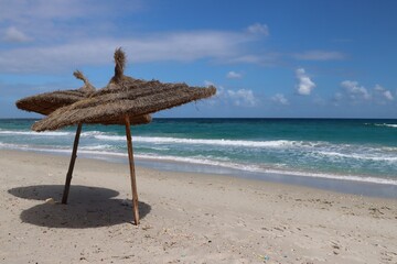 dwa parasole na brzegu morza piaszczysta plaża i błękit nieba.
