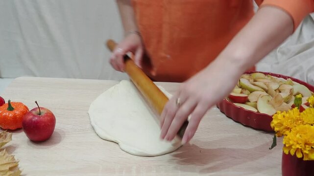 A girl is making apple pie at home. Autumn fall baking background with pumpkins, apples, nuts, food ingredients and seasonal spices. Cooking pumpkin or apple pie for Thanksgiving and autumn holidays, 