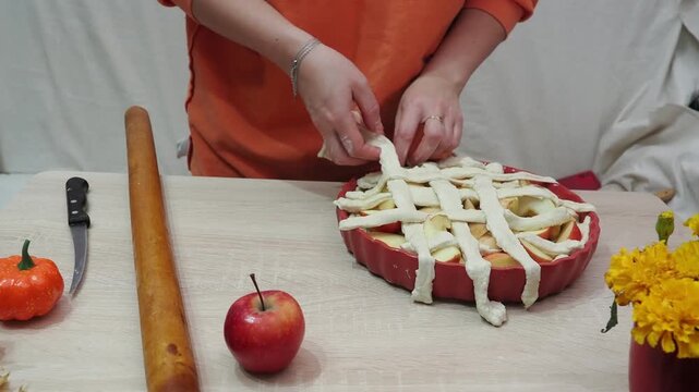 A girl is making apple pie at home. Autumn fall baking background with pumpkins, apples, nuts, food ingredients and seasonal spices. Cooking pumpkin or apple pie for Thanksgiving and autumn holidays, 