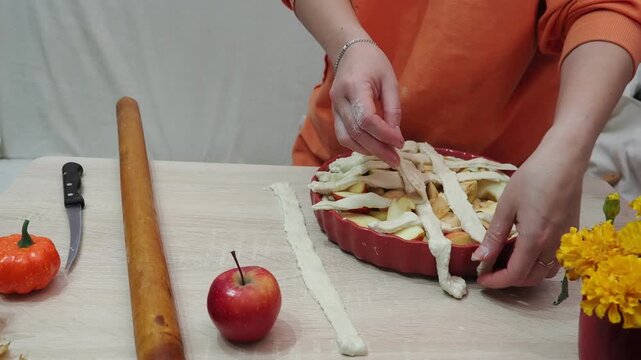 A girl is making apple pie at home. Autumn fall baking background with pumpkins, apples, nuts, food ingredients and seasonal spices. Cooking pumpkin or apple pie for Thanksgiving and autumn holidays, 