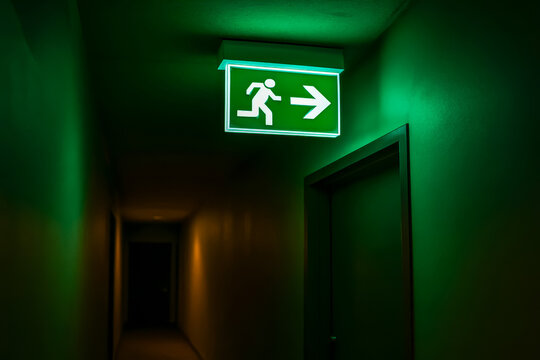 Green emergency exit sign illuminating a dark hallway
