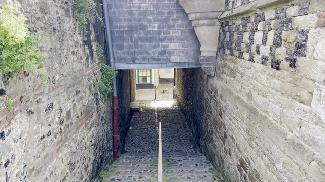 Narrow cobbled passage beneath Saint-Martin Church in Saint-Valery-sur-Somme, Picardy, descending under a slate-clad bridge between flint-and-limestone checkerboard walls, a medieval underpass