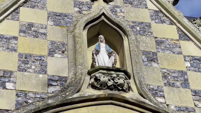 Gothic gable of Saint-Martin Church in Saint-Valery-sur-Somme, ornate finial and pointed niche holding a Virgin Mary statue set against flint-and-limestone checkerboard masonry under blue sky