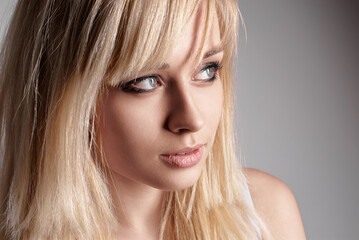 Naklejka premium Portrait capturing a young woman with blonde hair, gazing pensively, lit softly against a neutral backdrop.