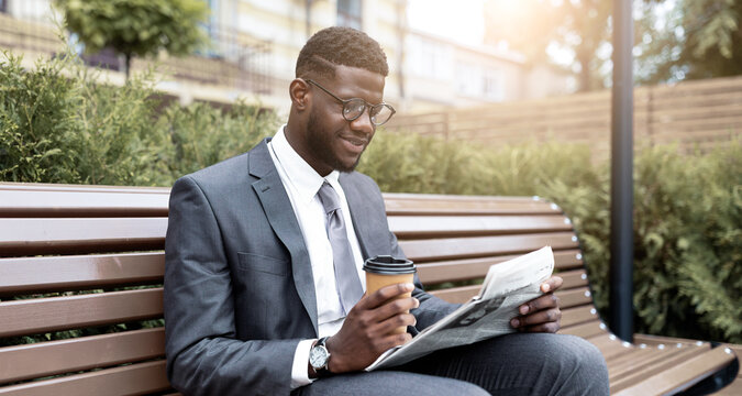 A well-dressed young man sits on a park bench while sipping coffee and reading a newspaper. The scene is bright and sunny, creating a relaxed atmosphere in the outdoor setting.