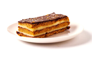 A dessert layered cake with chocolate is on a white plate on white background. The dessert is a cake with a brown crust. The plate is white and the dessert is the main focus of the image