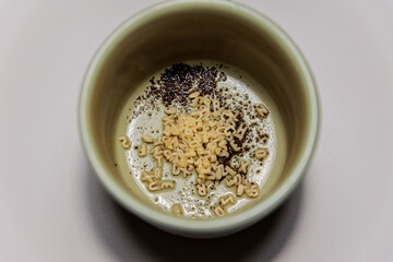 Close-up of a ceramic cup containing a mix of small alphabet-shaped pasta pieces and coffee grounds on a foamy surface, creating an abstract and artistic food composition