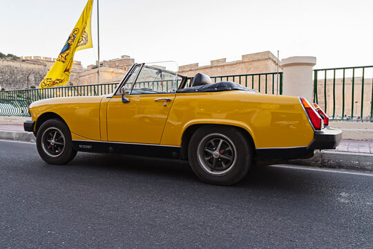 Classic MG Midget convertible parked on Maltese city street in soft daylight, chrome details and retro profile. British heritage and nostalgic automotive design: Kalkara, Malta - July 15, 2017