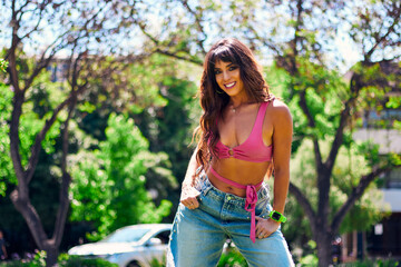 Beautiful, mature, Latina, Arab woman with dark hair, posing happily and inviting others to dance in an outdoor park. She's wearing a colorful retro pink outfit and jeans, and has makeup on. 