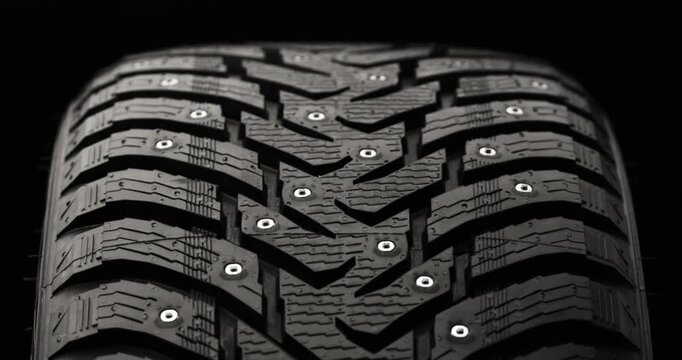 Studded winter tire rotating on black background, loop-ready