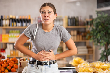 Young woman fidgeting by the stomach in the store. European woman felt unwell and indigestion in...