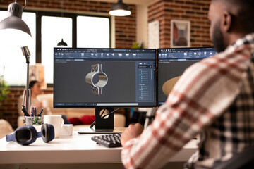 Creative male developer using cad software in brick wall apartment, designing 3d models for construction. African american man seated at workstation creating industrial tool prototypes in home studio.