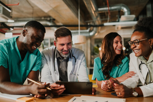 Diverse medical team collaborating on tablet, laughing together