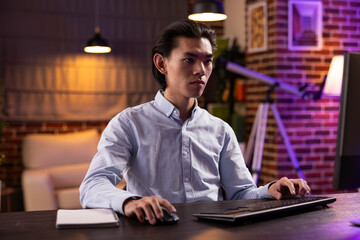 Serious entrepreneur sits at desk typing on computer keyboard, concentrating on remote freelance tasks. Dedicated asian man works from home, researching online strategies to develop business projects.