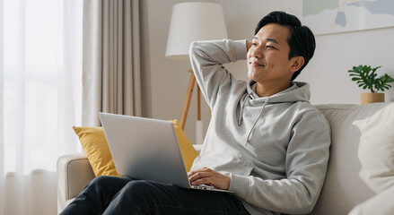 young asian man relaxing on sofa with laptop in cozy living room enjoying leisure time