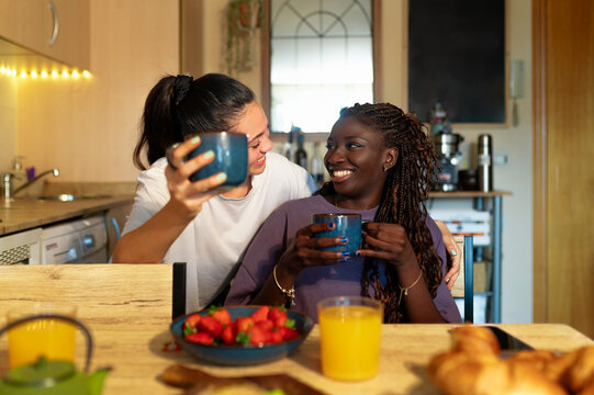 Happy lesbian couple enjoying morning breakfast, drinking coffee, and sharing a loving moment together at kitchen table