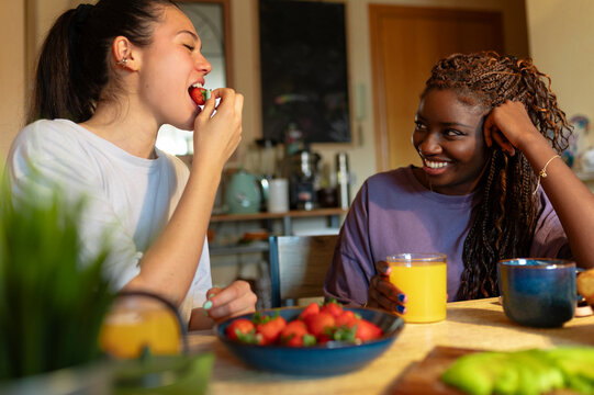 Two young women from a diverse lesbian couple sharing a happy morning breakfast with fresh strawberries and juice - Powered by Adobe