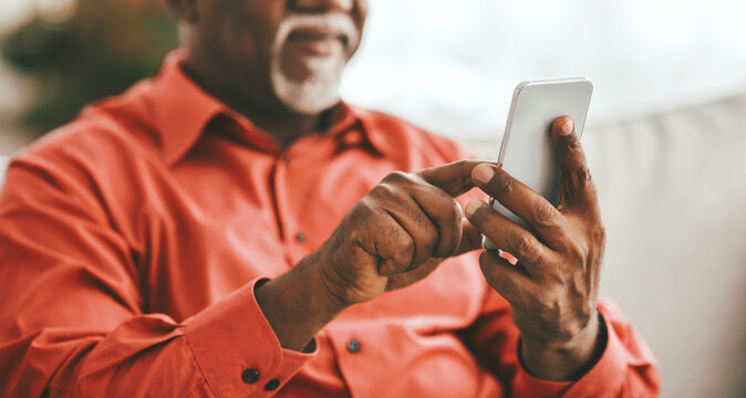 An older gentleman sits comfortably in a well-lit room, focused on his smartphone. He wears a vibrant red shirt and appears engaged in his activity, showcasing a moment of modern communication.