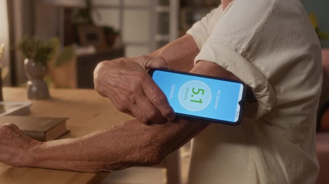 Side midsection shot of elderly female diabetes patient, dressed in short sleeve blouse, checking blood sugar with smartphone app and monitor patch on arm, getting good green reading