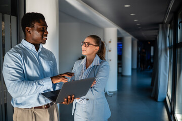 Business professionals collaborating with laptop in modern office hallway