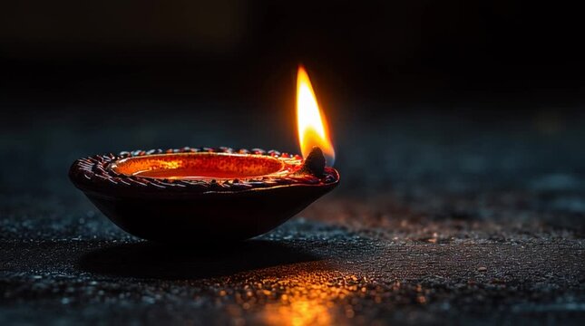 A close up view of a diya lamp with a bright flame illuminating the dark background and surface
