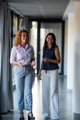 Two businesswomen walking together in modern office hallway