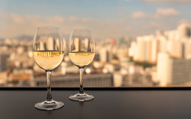 Two glasses of white wine on a table with a scenic view of the Seoul Korea city skyline under warm evening light, symbolizing romance, relaxation, and urban lifestyle.