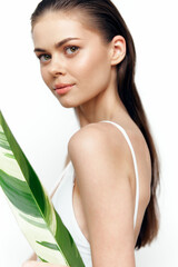 Young model with long hair holding a tropical leaf, showcasing a natural beauty portrait in minimalistic style, emphasizing freshness and elegance.