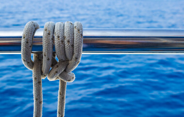 Close up of a rope tied in knot around metal rail, sea background